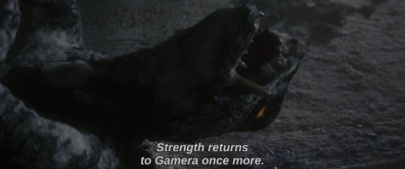 The monster Gamera, frozen in his battle with Barugon, begins to thaw. The subtitle reads, Strength returns to Gamera once more.
