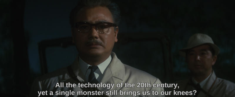 A scientist looks towards the camera in despair. An offscreen official says, All the technology of the 20th century, yet a single monster still brings us to our knees?