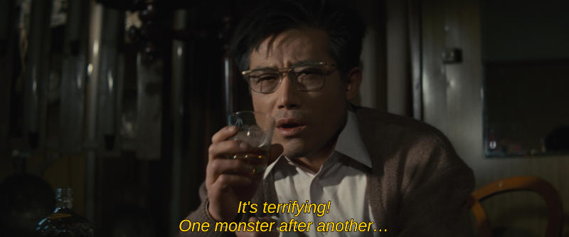 Color image. A man in glasses frightfully watches an offscreen television. The subtitle reads, It's terrifying! One monster after another...