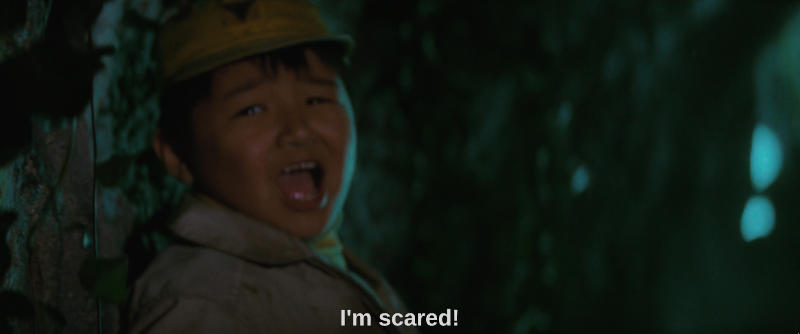A young boy stands against the wall of a cave, obviously frightened. The subtitle reads, I'm scared!.