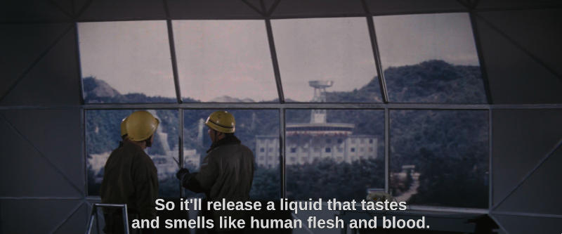 Several construction workers stand at a window, looking at a platform on top of a hotel in the distance. The subtitle reads, So it'll release a liquid that tastes and smells like human flesh and blood.